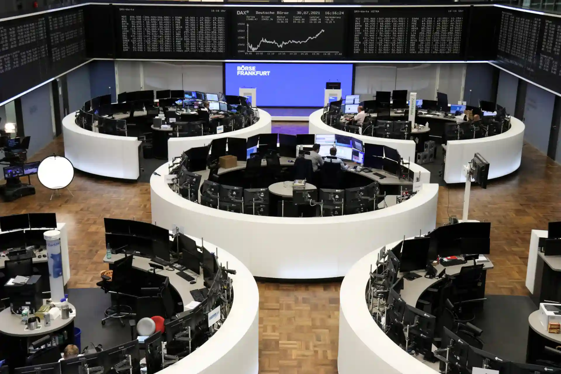 Sala de operações financeiras em um banco de Frankfurt com várias mesas de câmbio, telas e monitores exibindo dados do mercado financeiro.