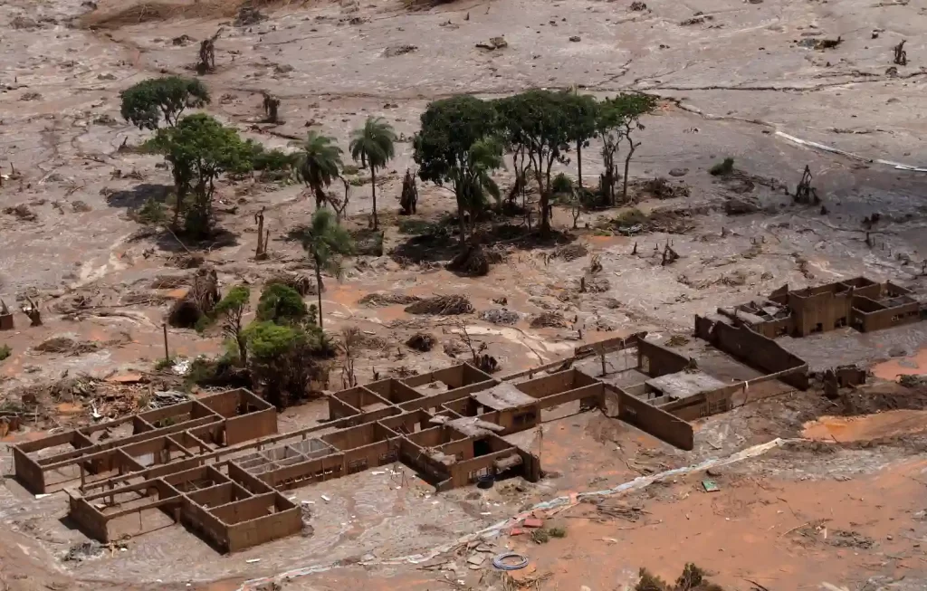 Imagem de uma área devastada por deslizamento de terra, com árvores destruídas e edificações parcialmente destruídas na região afetada, em um cenário de desastre natural.