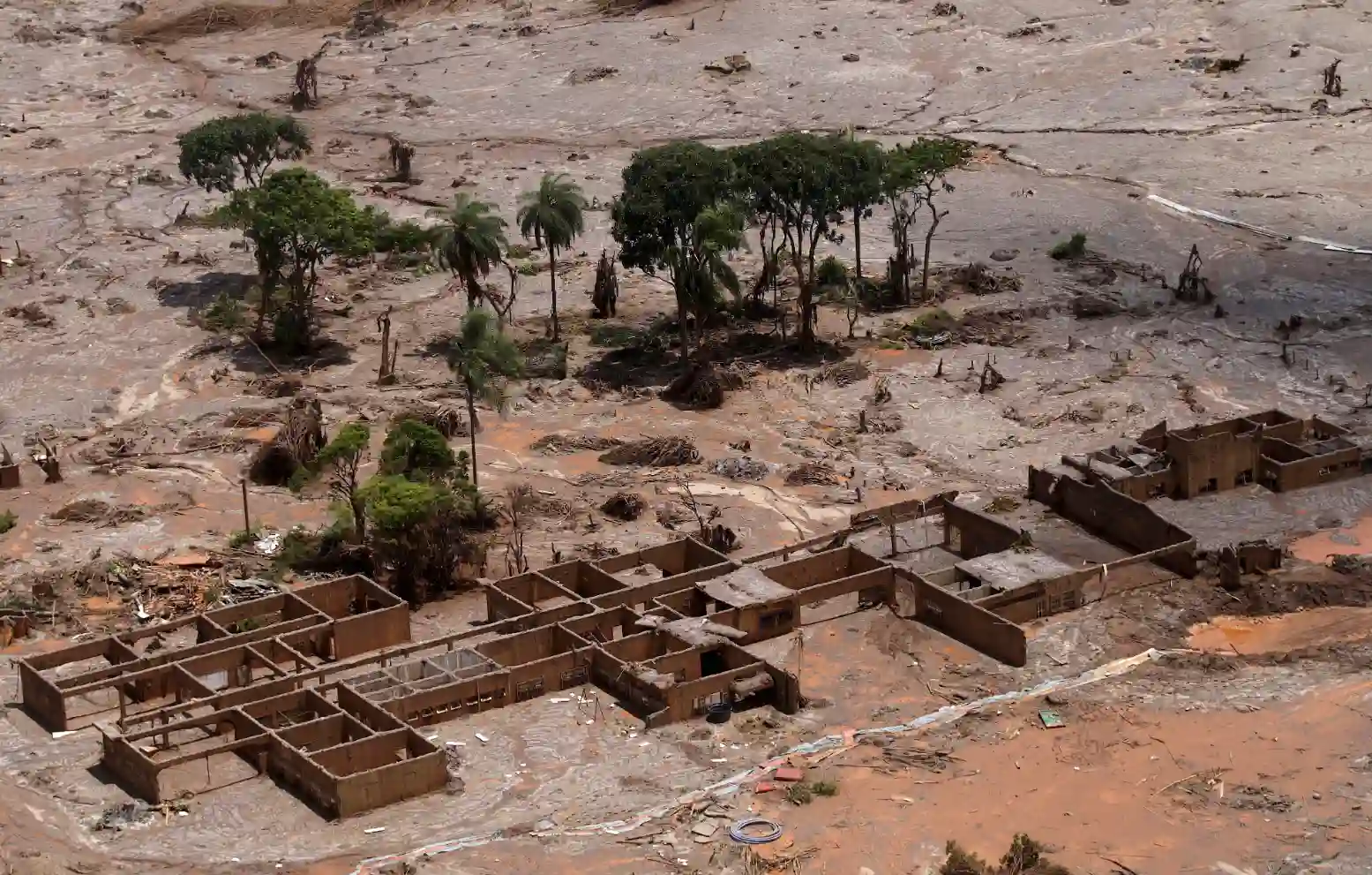 Imagem de uma área devastada por deslizamento de terra, com árvores destruídas e edificações parcialmente destruídas na região afetada, em um cenário de desastre natural.