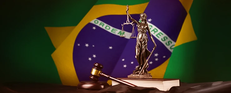 Imagem de uma balança de justiça ao lado de um livro e um martelo de juiz, com a bandeira do Brasil ao fundo, simbolizando o sistema jurídico brasileiro e o poder da justiça no país. Representando a independência do Brasil
