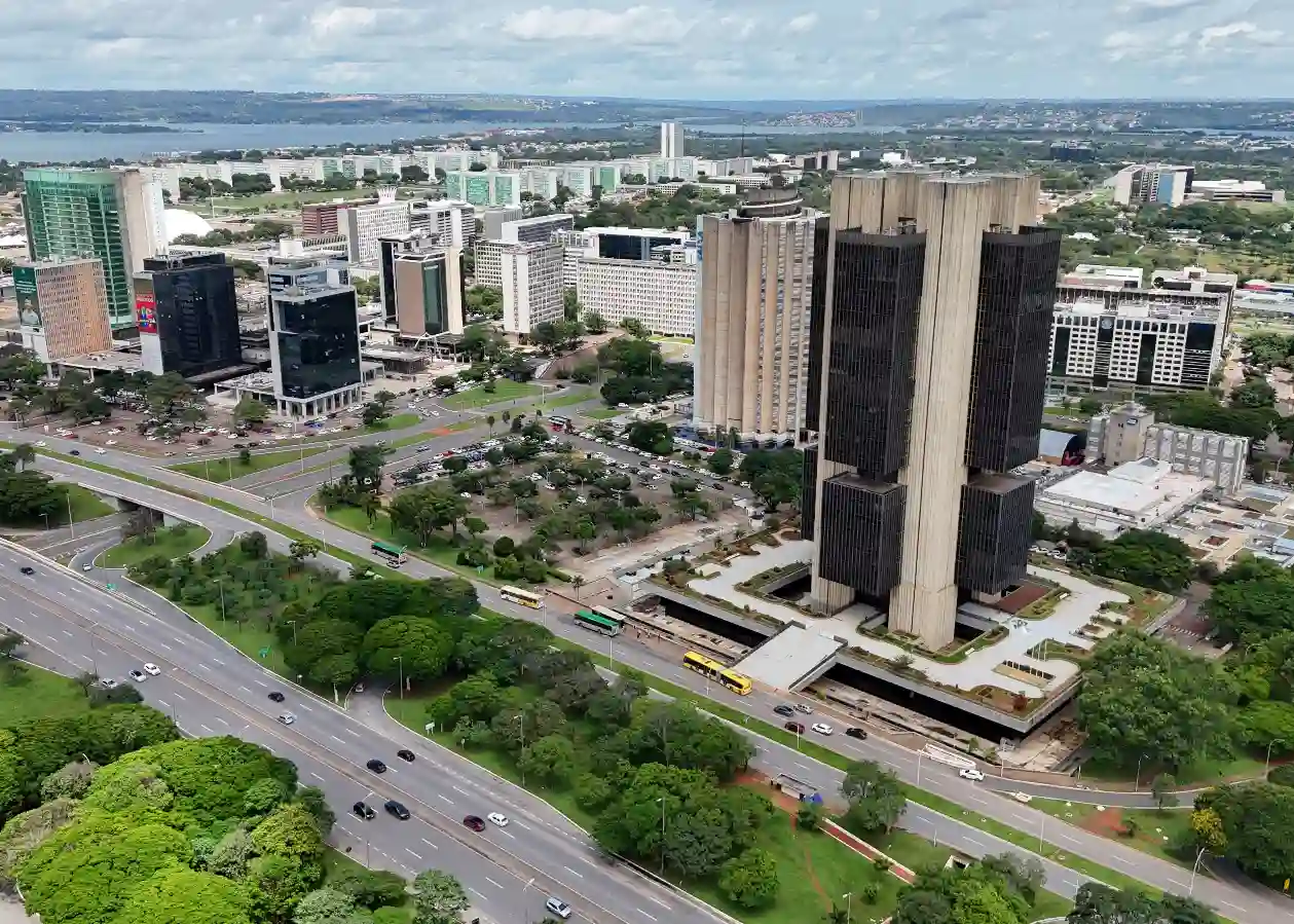 Imagem aérea de um centro urbano com arranha-céus modernos, áreas verdes e avenidas movimentadas, destacando um prédio alto e contemporâneo na cidade.