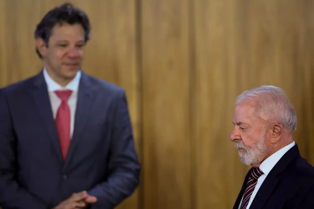 Homem mais jovem e homem mais velho em uma conversa formal, ambos usando ternos, com fundo de madeira, evidenciando um ambiente profissional.
