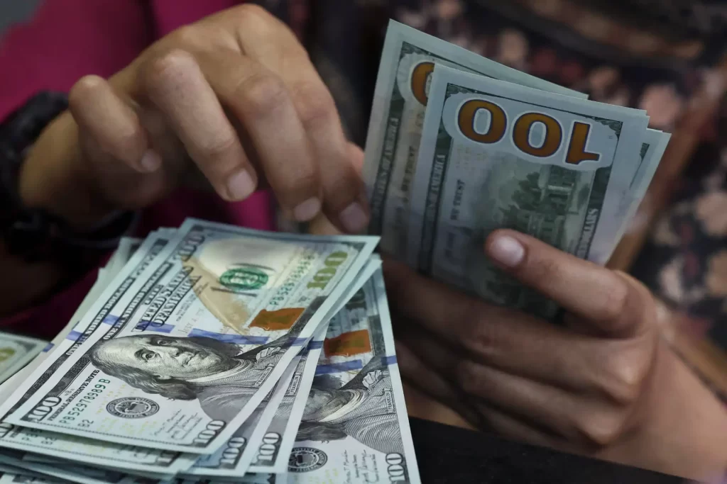 Pessoa segurando várias notas de dólar de 100 dólares, destacando o tema de dinheiro e riqueza.
