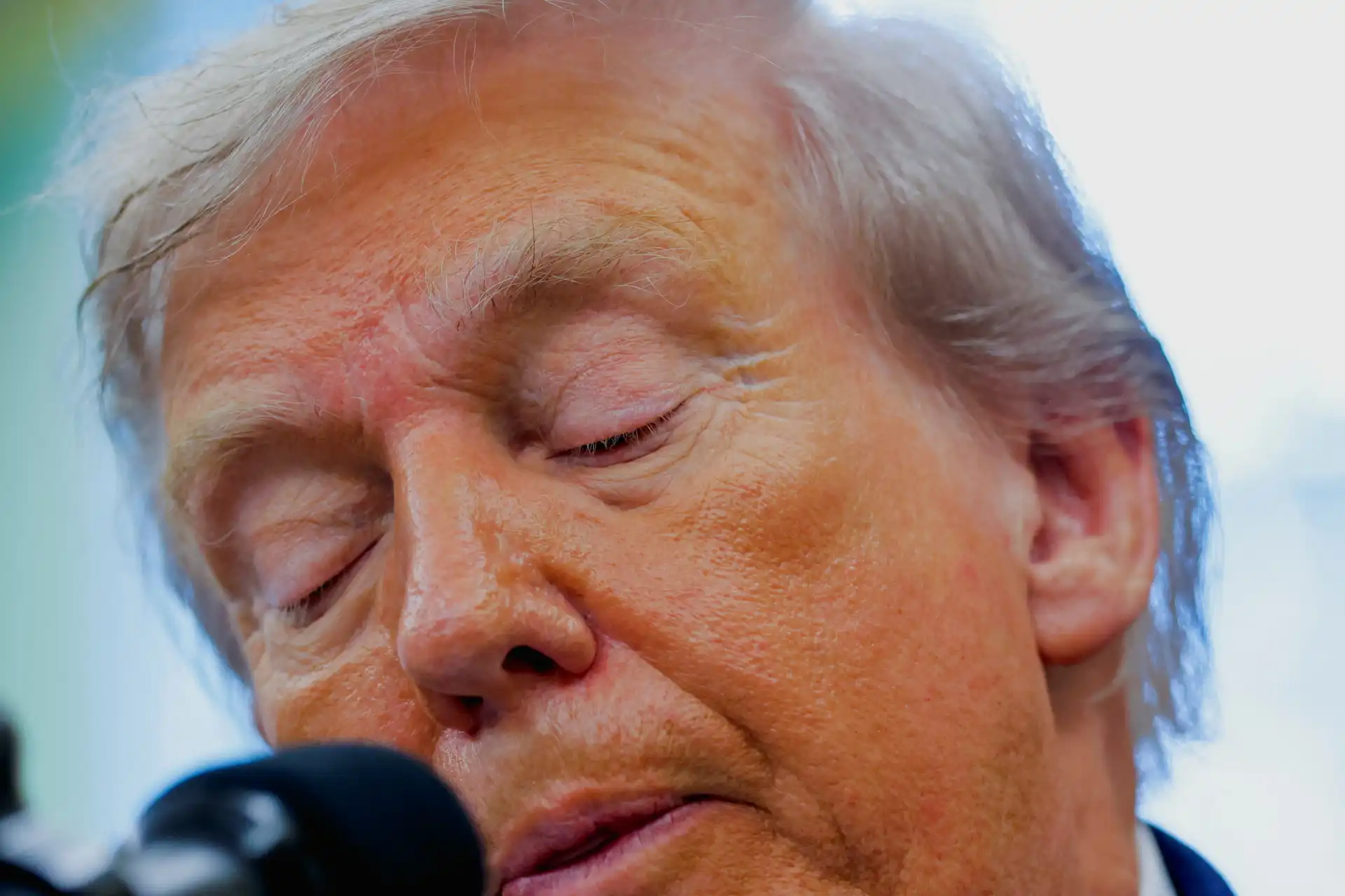 Imagem de Donald Trump com expressão pensativa, olhos fechados, cabelos grisalhos e pele com tonalidade laranja, em uma ocasião pública.
