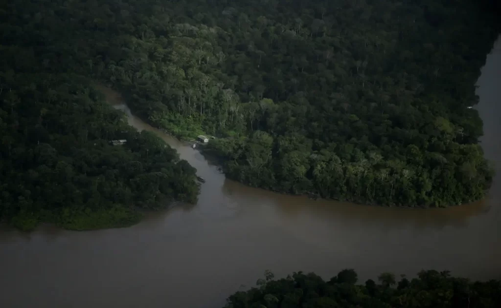 Imagem de uma área de floresta ao redor de um rio de grande porte com águas marrons, destaque para a preservação ambiental da Amazônia.