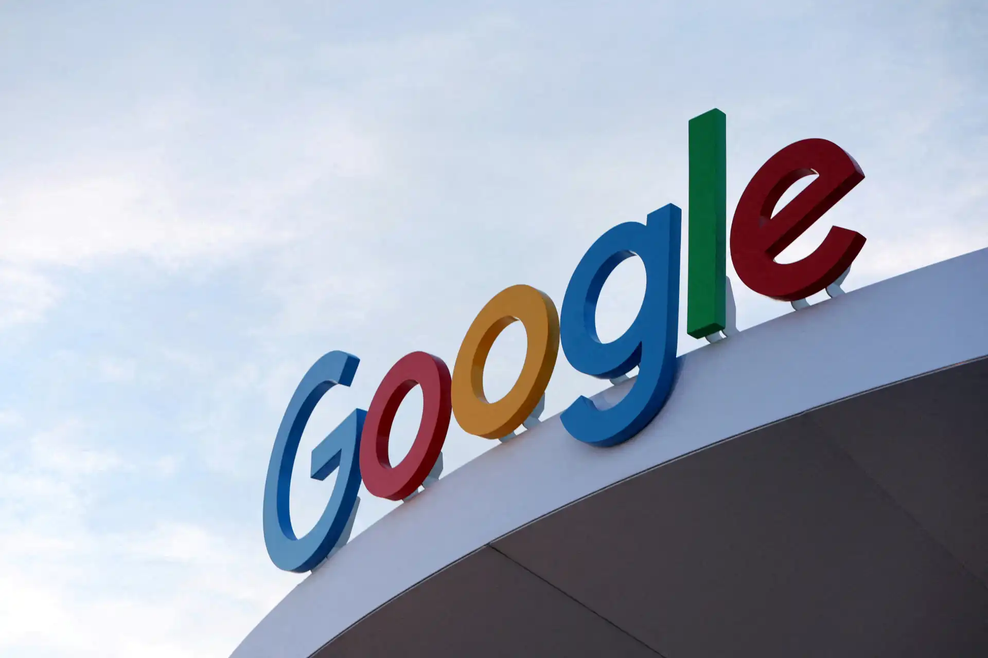 Logotipo da Google em cores vibrantes na fachada de uma loja ou escritório com céu ao fundo, simbolizando inovação e tecnologia.