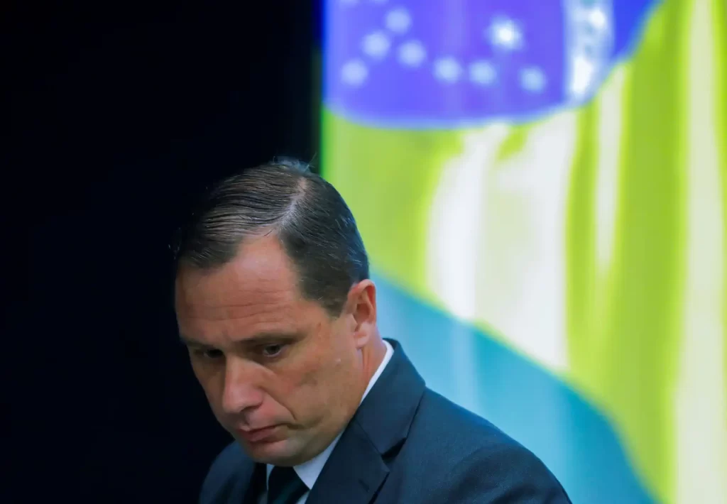 Homem sério em traje formal, com expressão pensativa, em ambiente com fundo colorido, apresentando uma atmosfera de reflexão ou concentração.