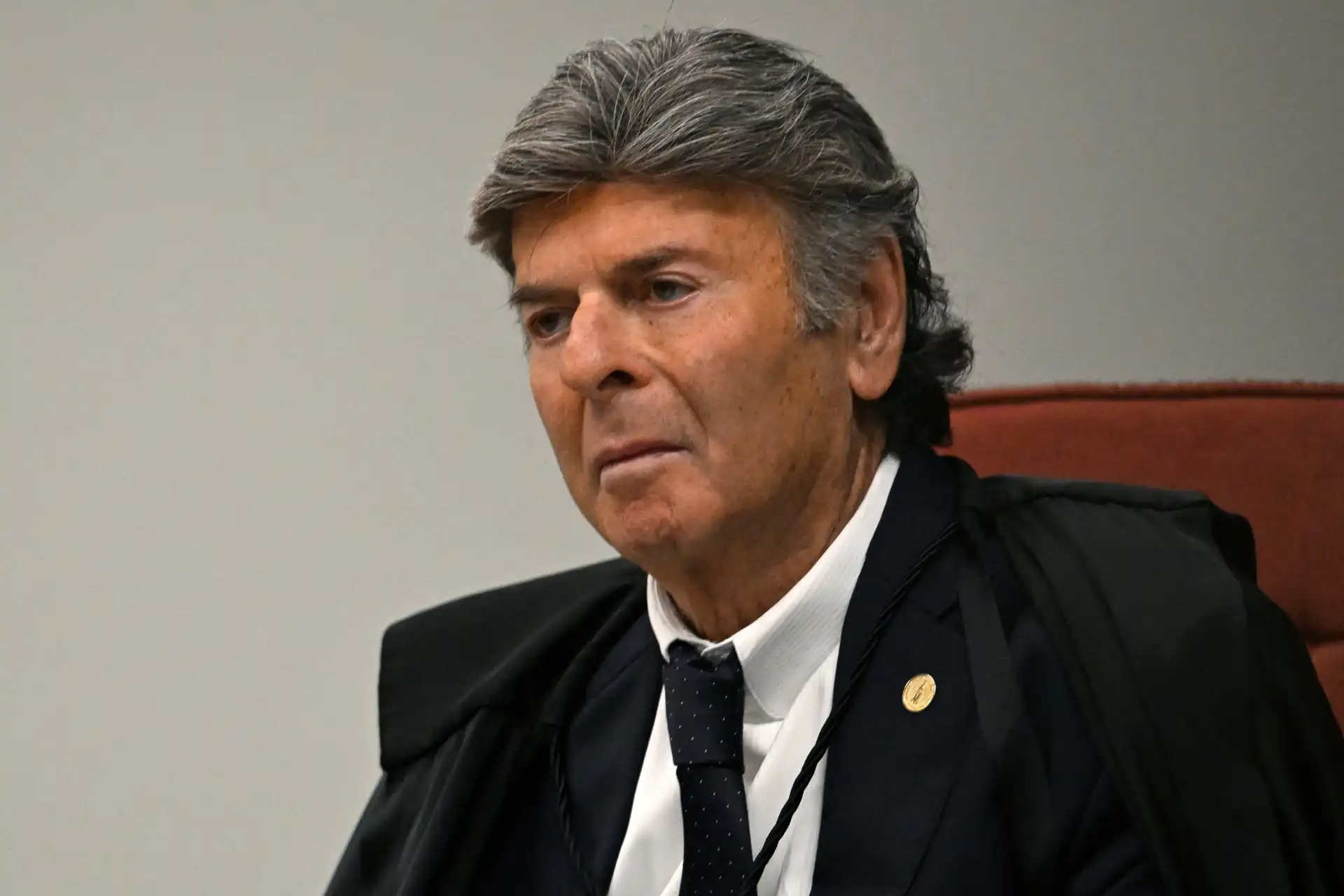 Imagem de um juiz de toga preta e com cabelo grisalho, sentado em uma sala de tribunal, demonstrando seriedade e concentração, em um ambiente formal.