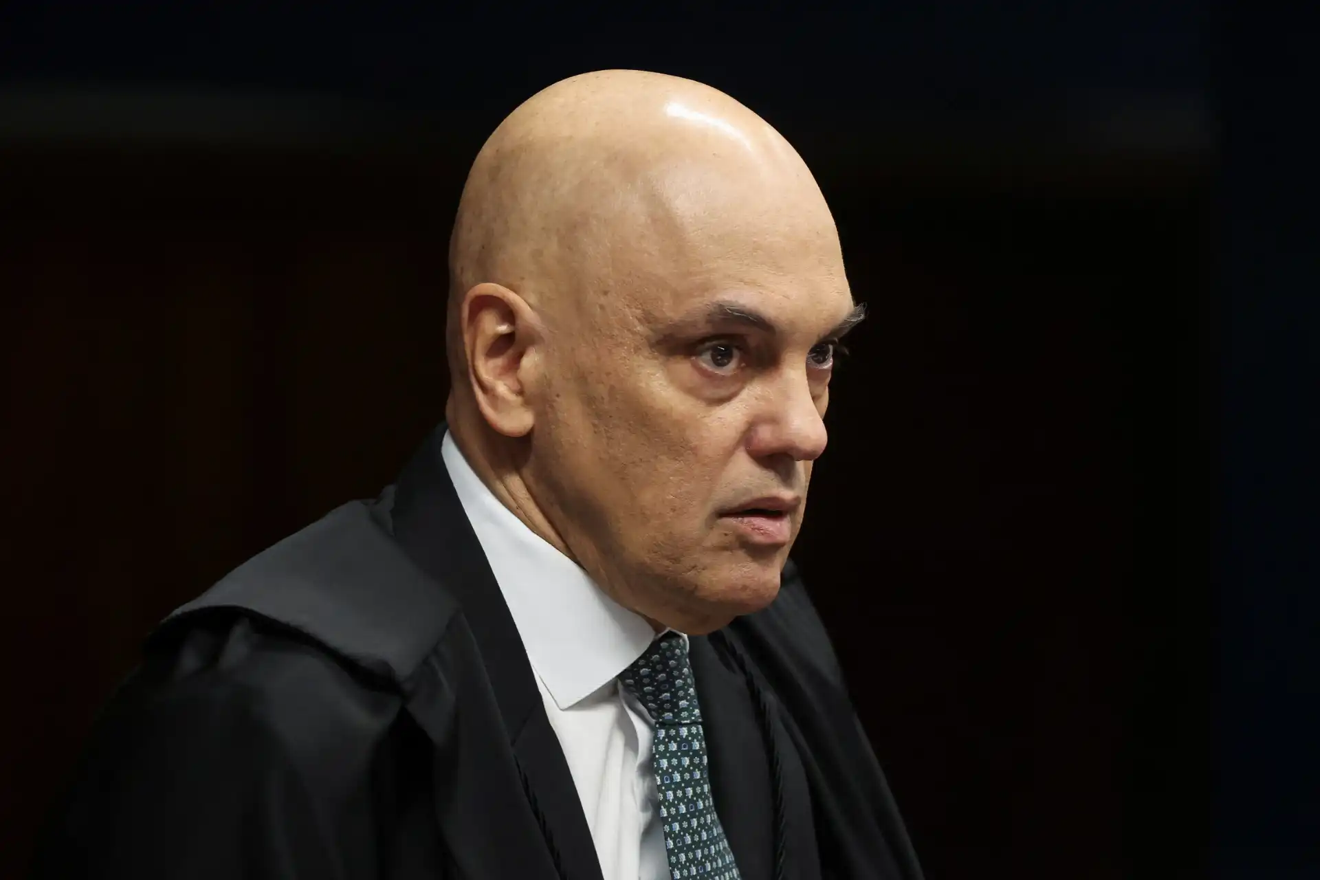 Juiz de tribunal com expressão séria, vestindo toga preta, em ambiente de sala de audiência, simbolizando justiça e autoridade judicial.