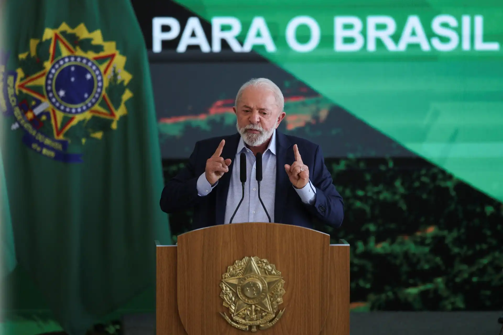 Luiz Inácio Lula da Silva durante discurso oficial no Brasil, na presença da bandeira nacional, usando terno, com expressão séria e gesticulando com as mãos, destacando a importância da política brasileira.
