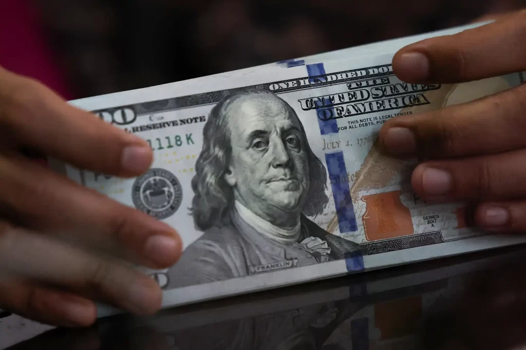 Mãos segurando uma nota de cento dólares americanos com a imagem de Benjamin Franklin.