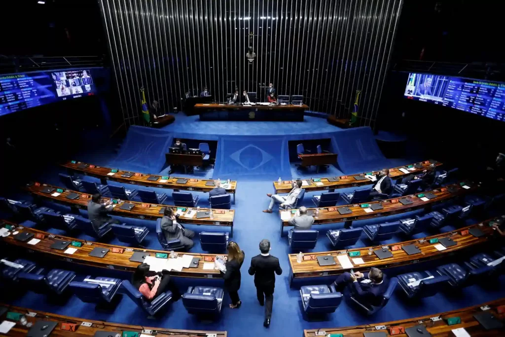 Plenário do Congresso Nacional do Brasil com senadores e deputados em reunião, ambiente formal e organizado, com o símbolo do Brasil ao centro do palco, e telas com informações ao fundo.