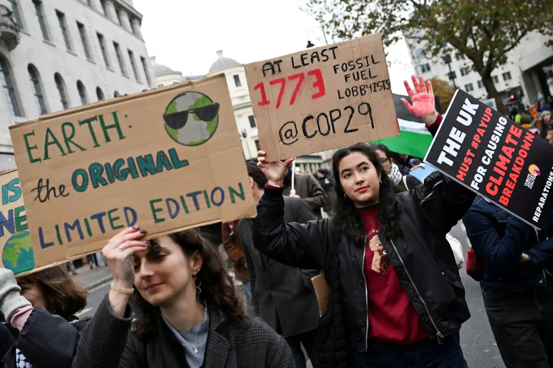 Protesto climático com jovens segurando placas contra uso de combustíveis fósseis e apoiando o clima, movimento ambientalista no centro da cidade.
