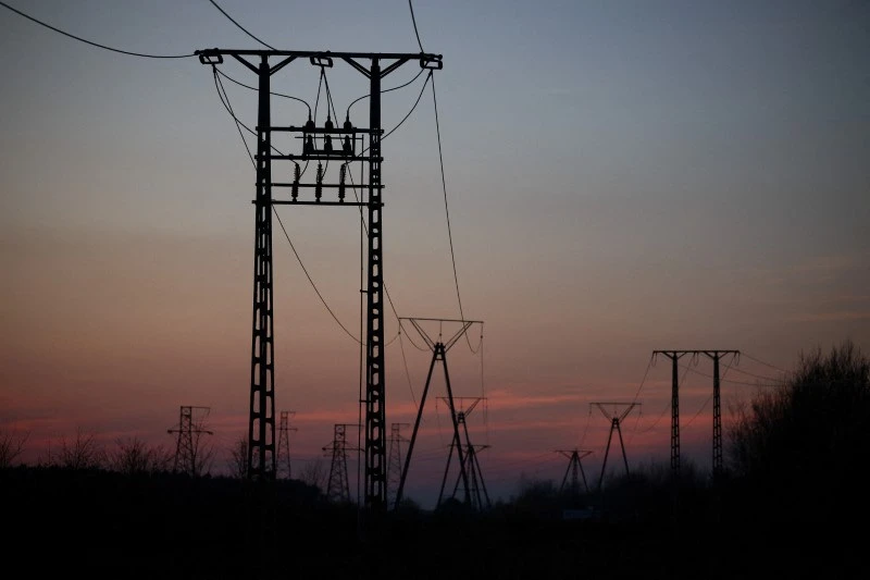 Imagem de torres de transmissão de energia elétrica ao pôr do sol, com céu colorido ao fundo, representando infraestrutura de energia.