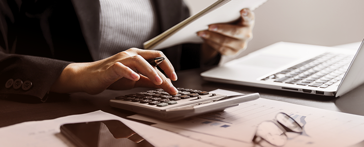 Pessoa trabalhando com planilhas e computador portátil para análise financeira ou administrativa, focando em produtividade e organização.