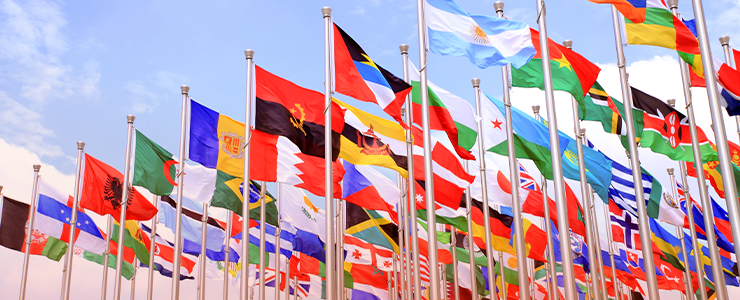 Imagem de várias bandeiras de países diferentes ao vento sob céu claro, representando diversidade e união internacional.