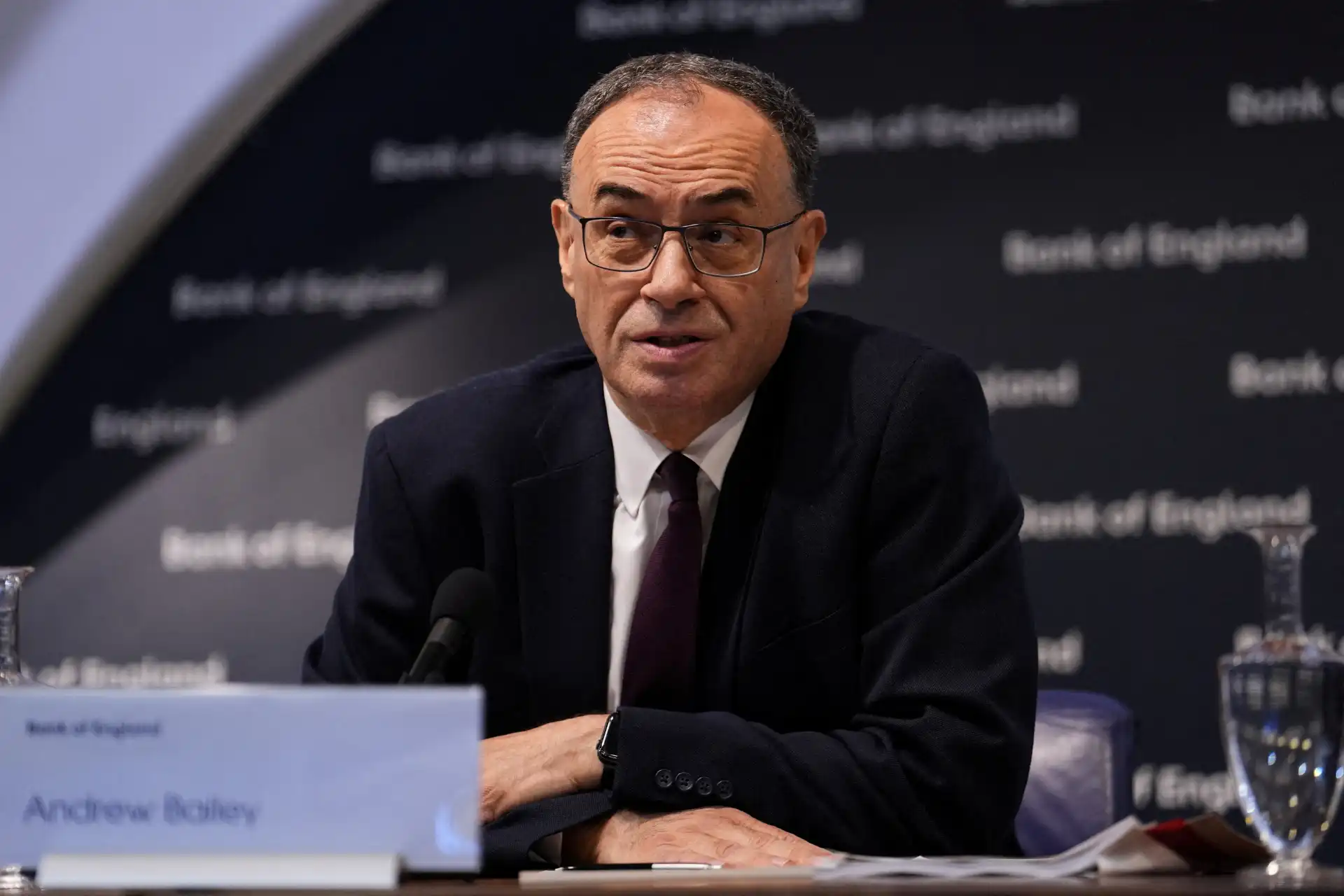 Andrew Bailey, presidente do Banco da Inglaterra, em uma conferência de imprensa, usando terno e óculos, falando ao microfone.