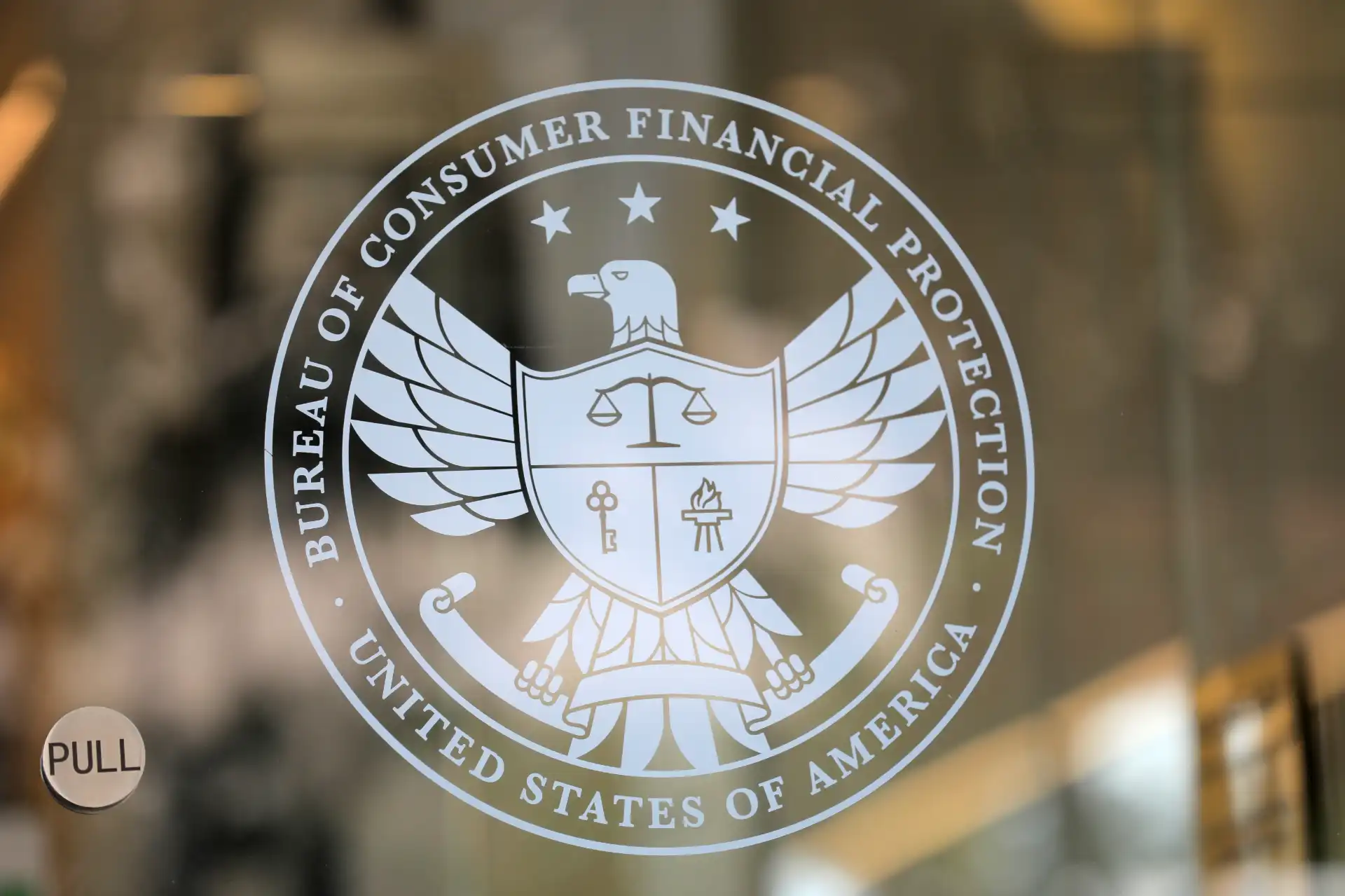 Emblema da Bureau of Consumer Financial Protection dos Estados Unidos, com símbolo de águia, escudo, balança, chave e vela, representando proteção ao consumidor e regulação financeira.