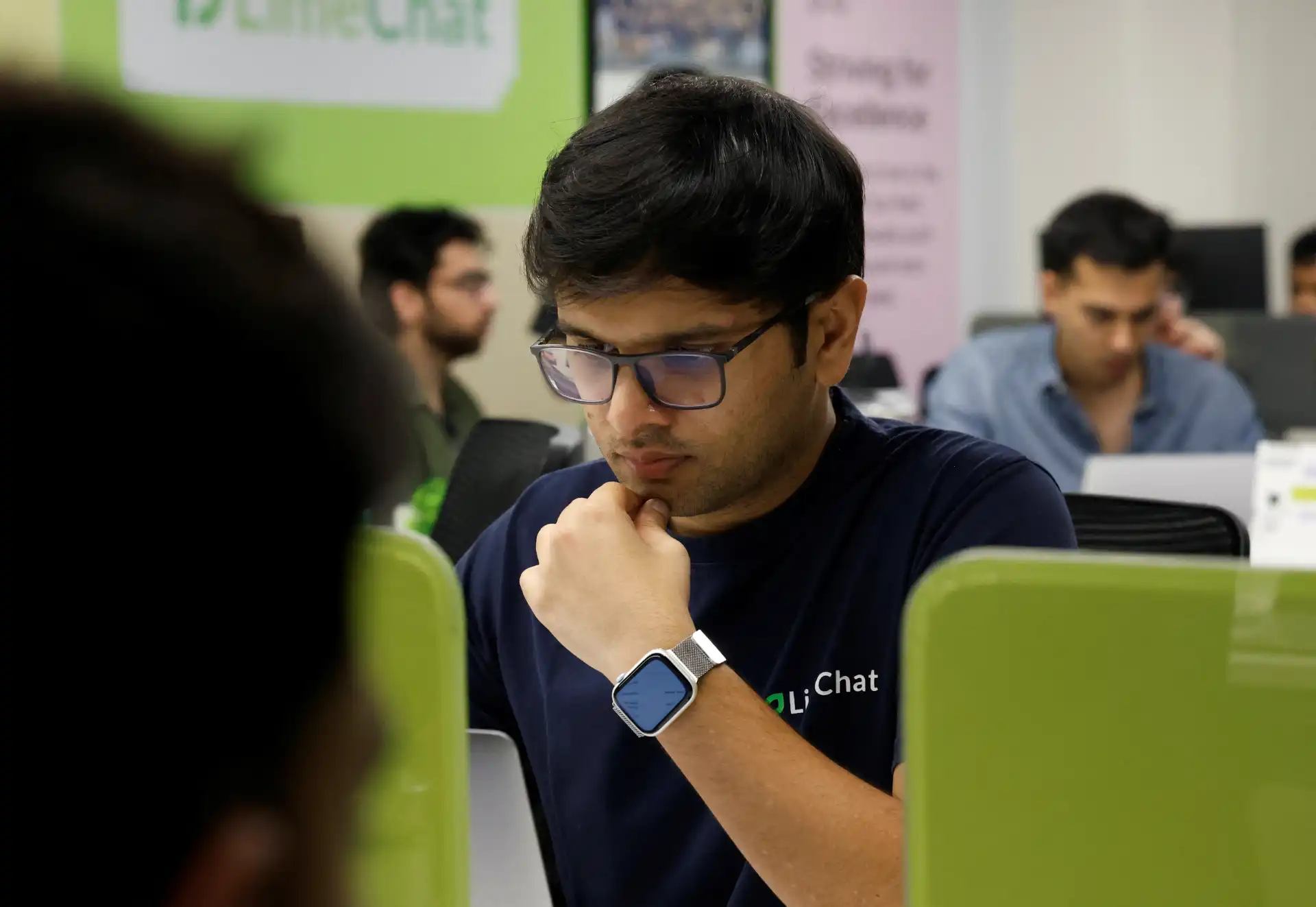 Homem usando óculos e smartwatch no ambiente de coworking, concentrado talvez em uma reunião ou trabalho.