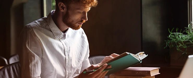 Homem lendo um livro em um ambiente com iluminação suave, estilo de vida de estudante ou profissional, buscando ampliar conhecimentos ou relaxar na leitura.