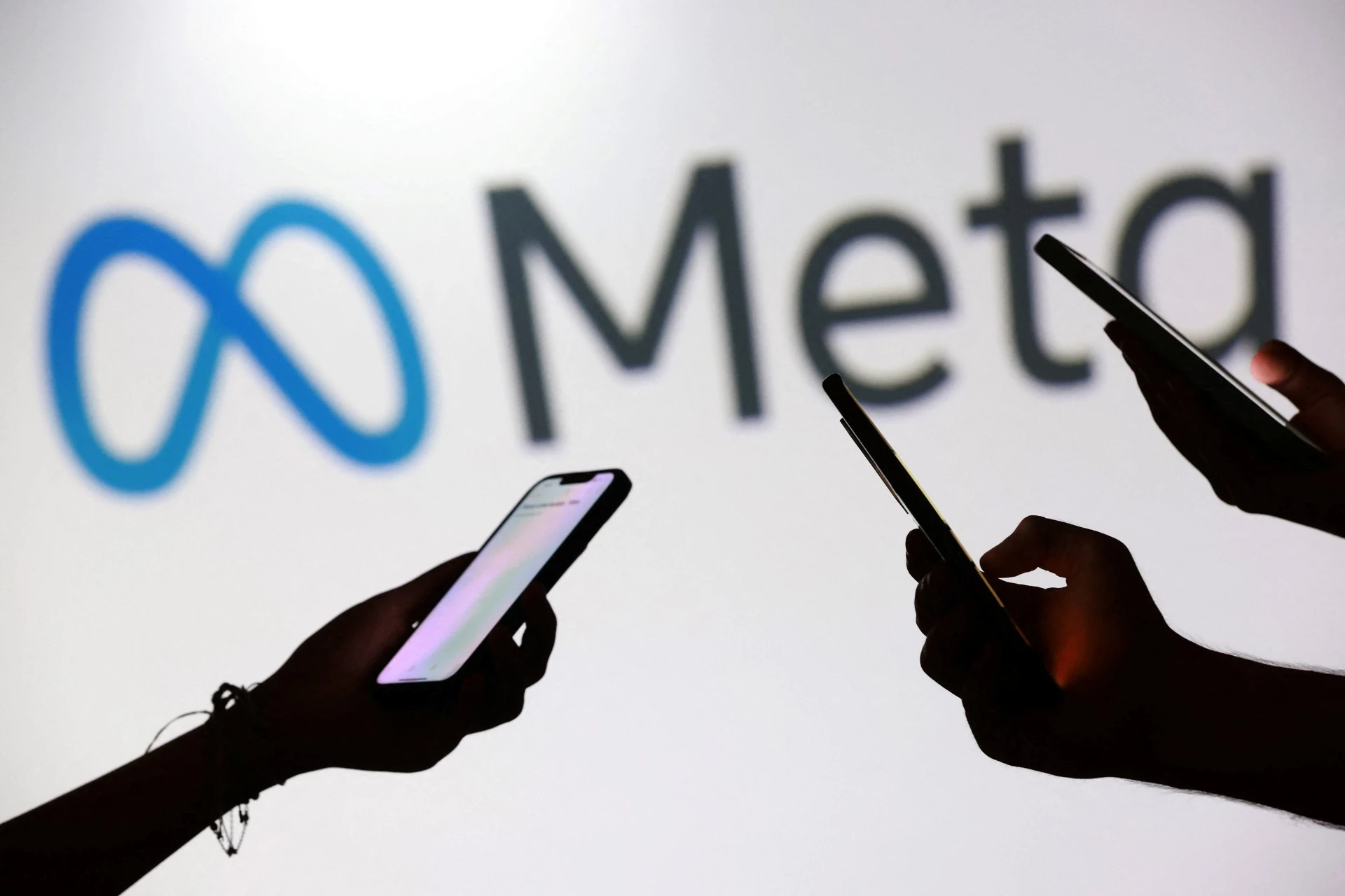 Pessoas usando smartphones em frente ao logo do Meta, empresa de tecnologia, redes sociais e metaverso.