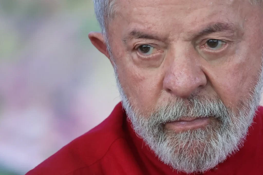 Imagem de Luiz Inácio Lula da Silva, presidente do Brasil, com expressão séria, cabelos grisalhos e barba grisalha, usando uma blusa vermelha.