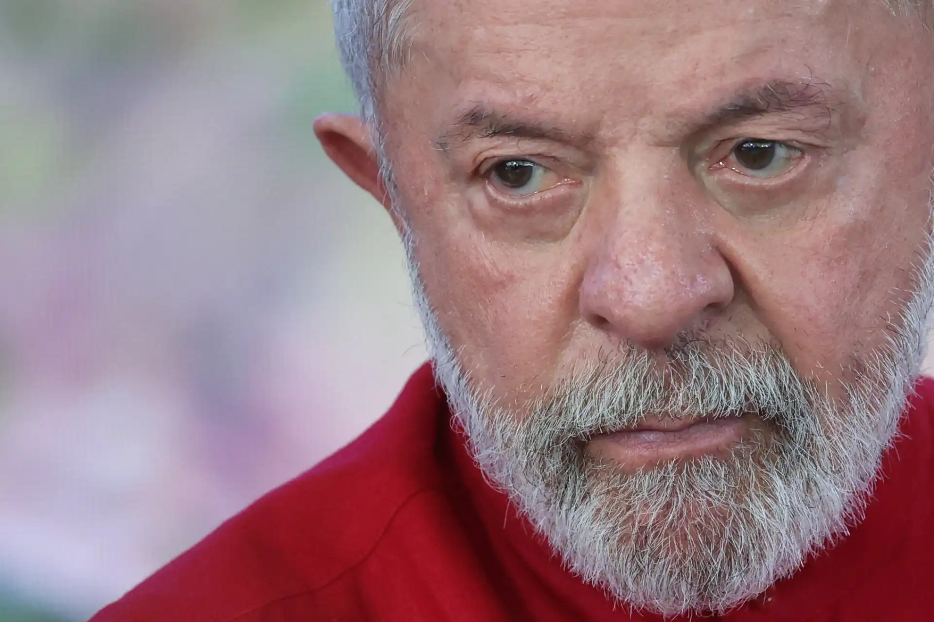 Imagem de Luiz Inácio Lula da Silva, presidente do Brasil, com expressão séria, cabelos grisalhos e barba grisalha, usando uma blusa vermelha.