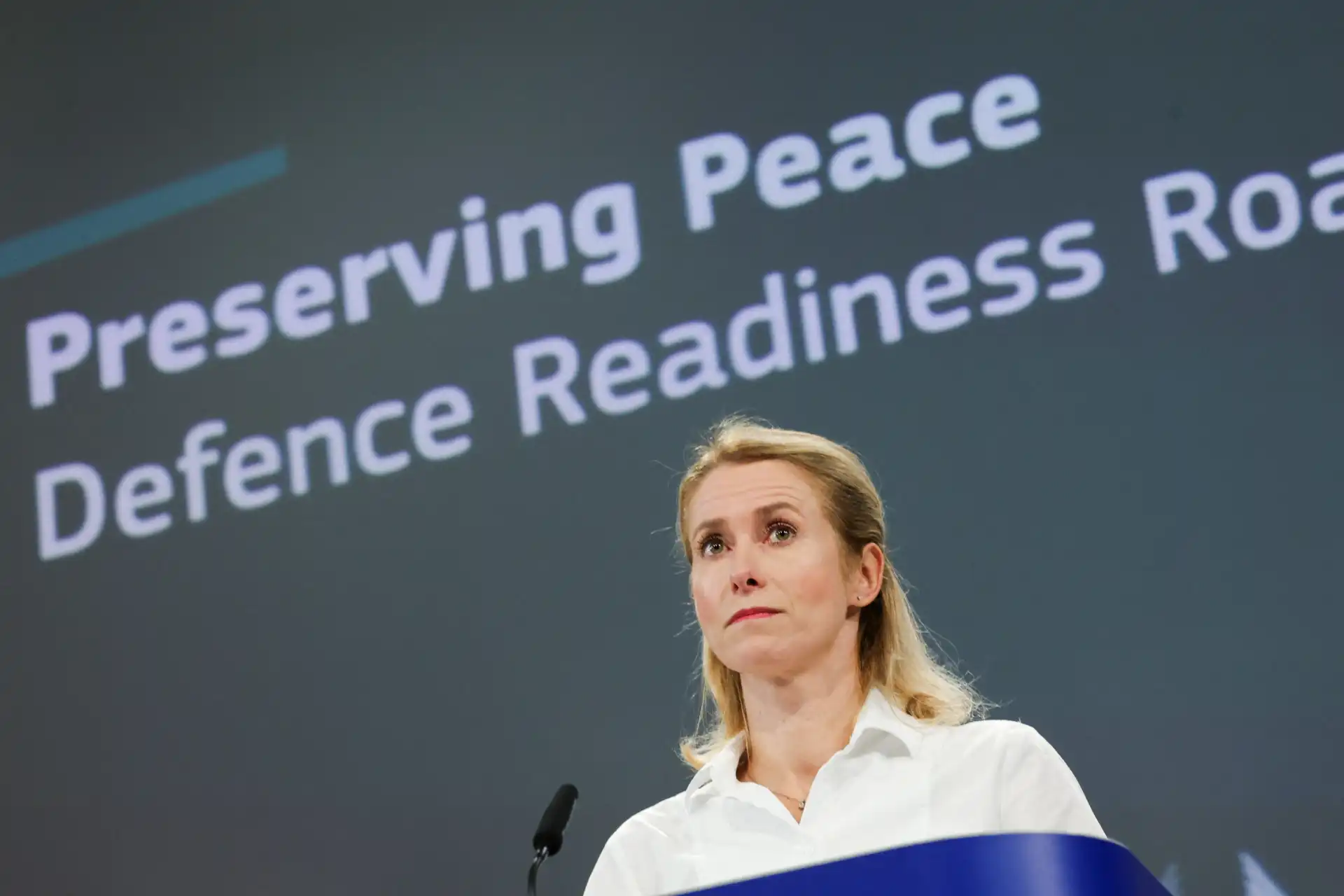 Mulher fazendo discurso na conferência 'Preserving Peace Defence Readiness' com fundo que mostra a frase no painel.
