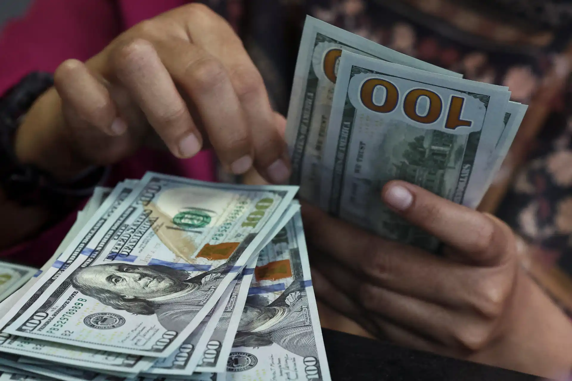 Pessoa contando e trocando notas de US$100, destaque para as notas de cem dólares em uma transação financeira.