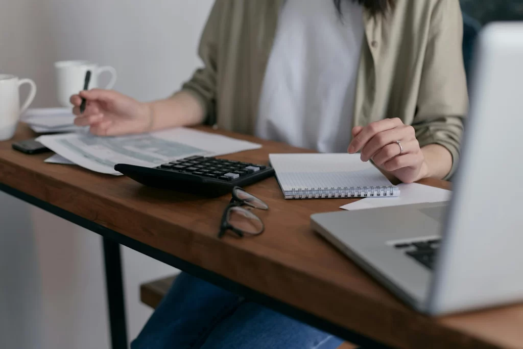 Pessoa trabalhando em um escritório com computador, calculadora, blocos de notas e papéis na mesa, ambiente de trabalho organizado. reforma tributária