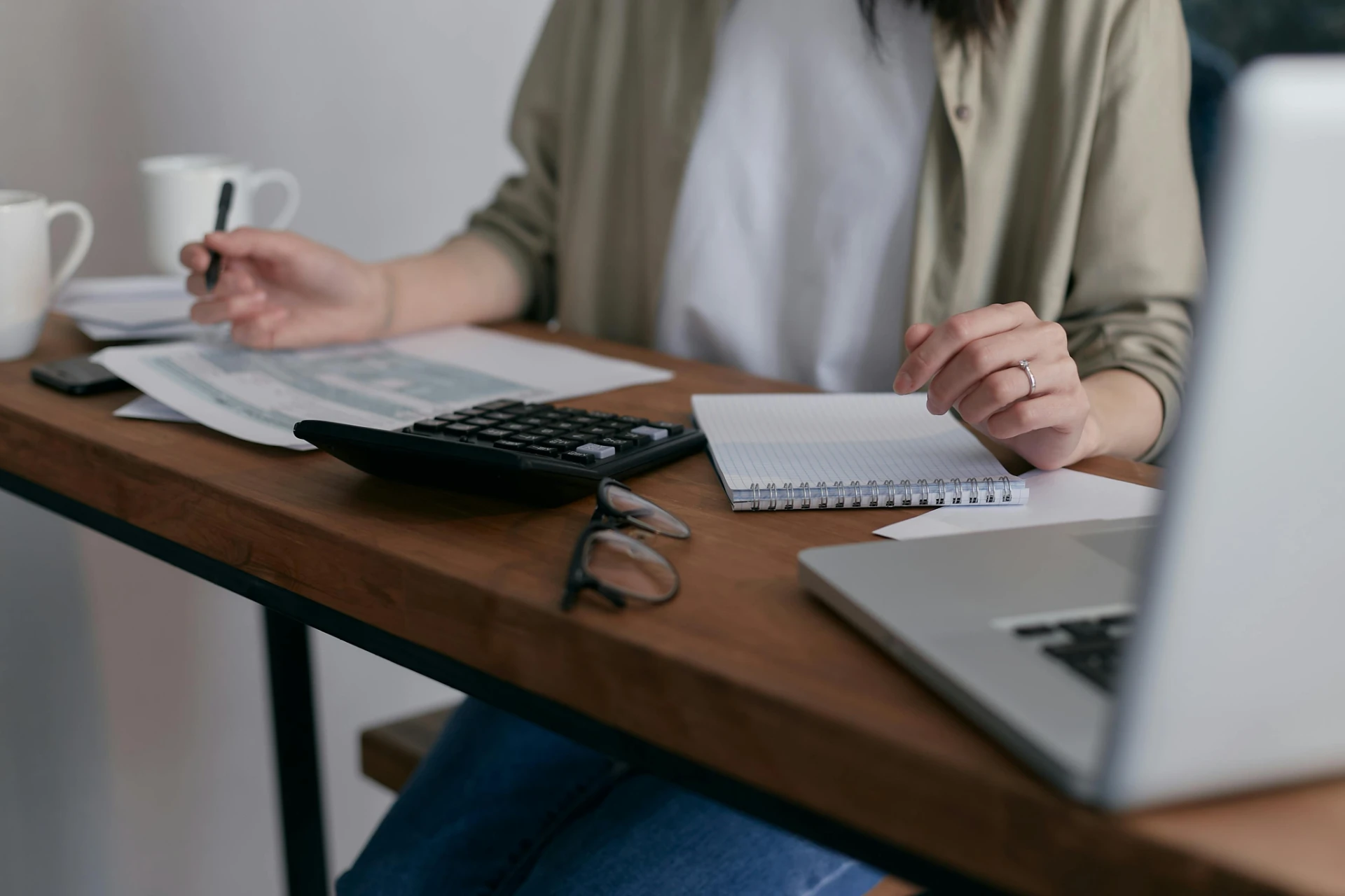 Pessoa trabalhando em um escritório com computador, calculadora, blocos de notas e papéis na mesa, ambiente de trabalho organizado. reforma tributária