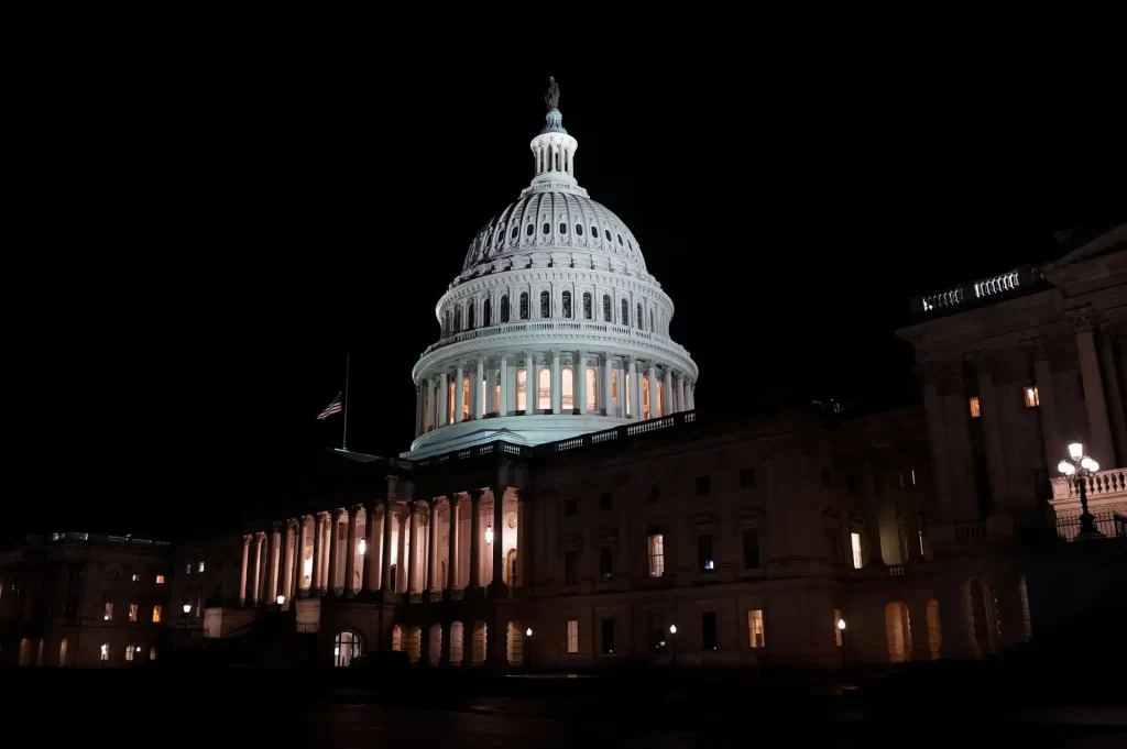 Imagem do Capitólio dos Estados Unidos iluminado à noite, com destaque para sua cúpula icônica em Washington D.C. símbolo de poder e democracia americana.