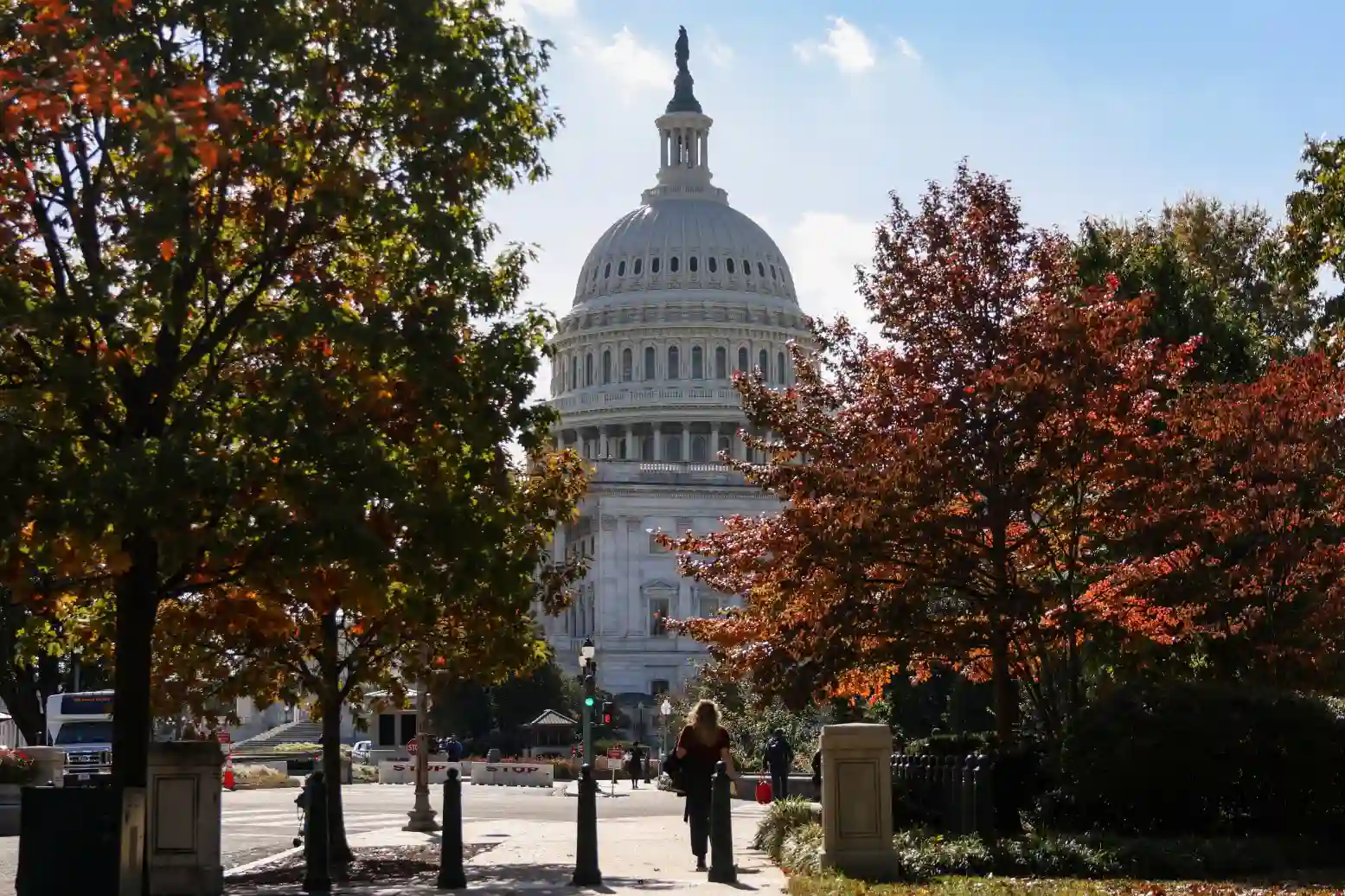 Imagem da Casa do Capitólio, símbolo de Washington, com árvores de outono ao redor, pessoas caminhando na frente, um dia ensolarado para visitações.