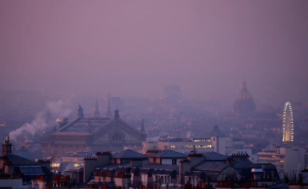 Vista panorâmica de Londres ao entardecer, mostrando prédios históricos, uma roda gigante iluminada e uma atmosfera com céu lilás e enevoado.