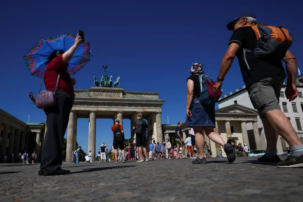 Turistas visitando a Porta de Brandemburgo em Berlim, na Alemanha, com céu claro e pessoas explorando a cidade.