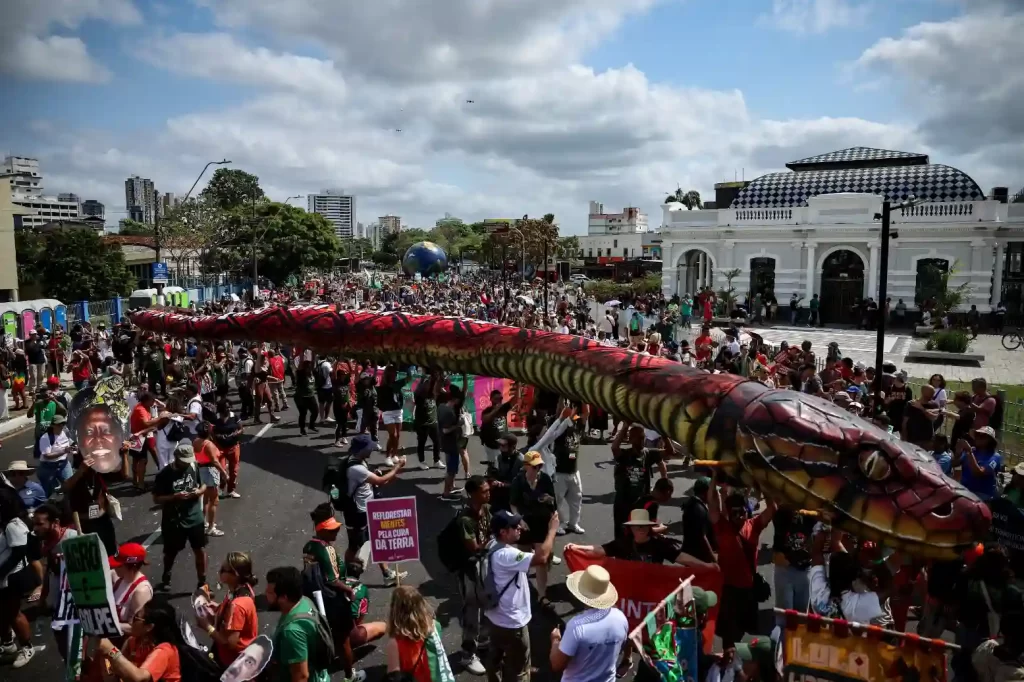 Protesto com grande mobilização na cidade, destacando uma grande cobra colorida vivendo em uma manifestação de rua, com muitas pessoas