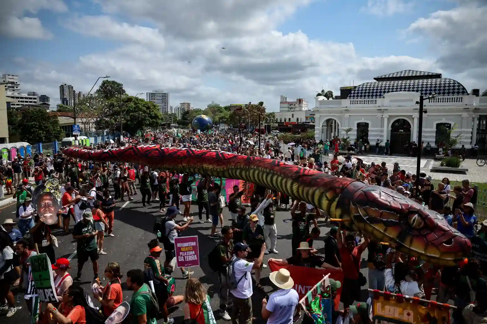 Protesto com grande mobilização na cidade, destacando uma grande cobra colorida vivendo em uma manifestação de rua, com muitas pessoas