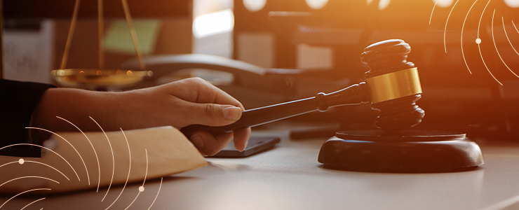Imagem de um martelo de juiz sobre uma mesa de tribunal, simbolizando justiça e lei, com iluminação quente ao fundo. Representa o sistema judicial e processos legais.