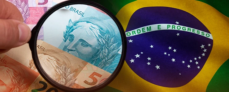 Análise de notas de dinheiro brasileiro com uma lupa na bandeira do Brasil ao fundo, destacando a segurança e autenticidade da moeda nacional.