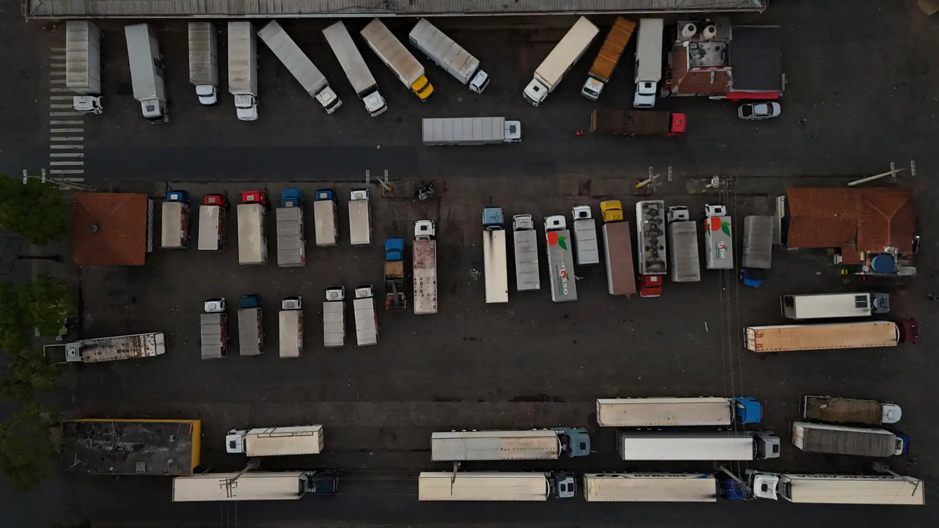 Imagem aérea de caminhões de carga e veículos estacionados em pátio de transporte, com destaque para a logística de entrega e distribuição de mercadorias.