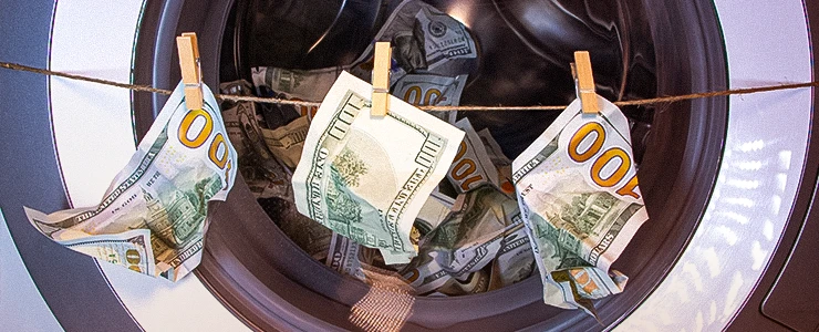Dinheiro de cem dólares sendo lavado na máquina de lavar roupas, representando a lavagem de dinheiro, com notas americanas de $100 penduradas em roupas de varal.