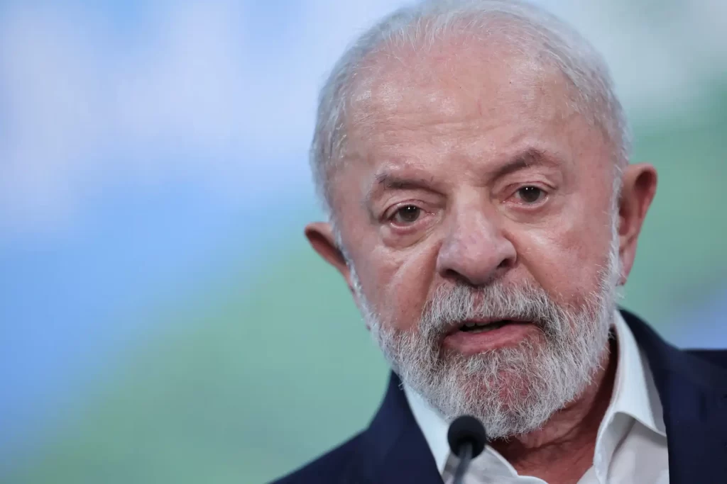 Imagem do ex-presidente Lula durante discurso, com expressão séria e cenário desfocado ao fundo.