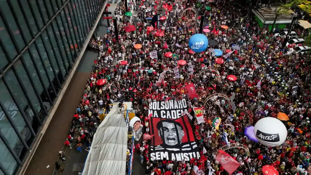 Grande manifestação na rua com milhares de pessoas participando de um protesto político, muitos com cartazes e bandeiras contra Bolsonaro.