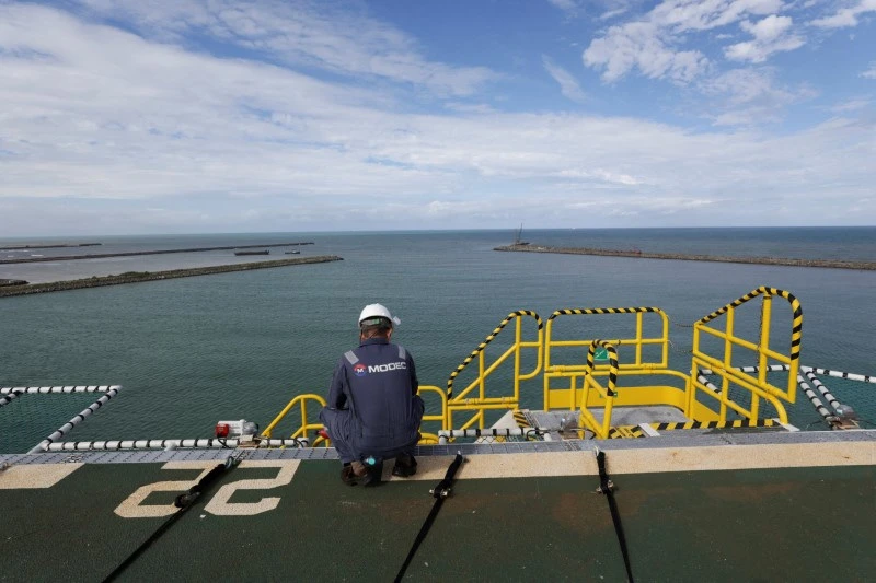 Técnico em manutenção de plataformas marítimas observa o mar e equipamentos de segurança na estrutura de uma plataforma de petróleo ou energia offshore.