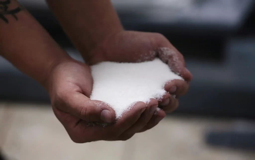 Mãos segurando açúcar em pó, destaque para a textura fina e o momento de manipulação do ingrediente culinário.