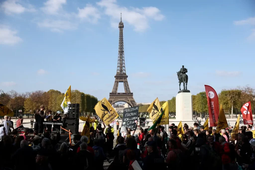 Protesto em Paris com pessoas segurando bandeiras e cartazes na frente da Torre Eiffel, marcando manifestação política na França.