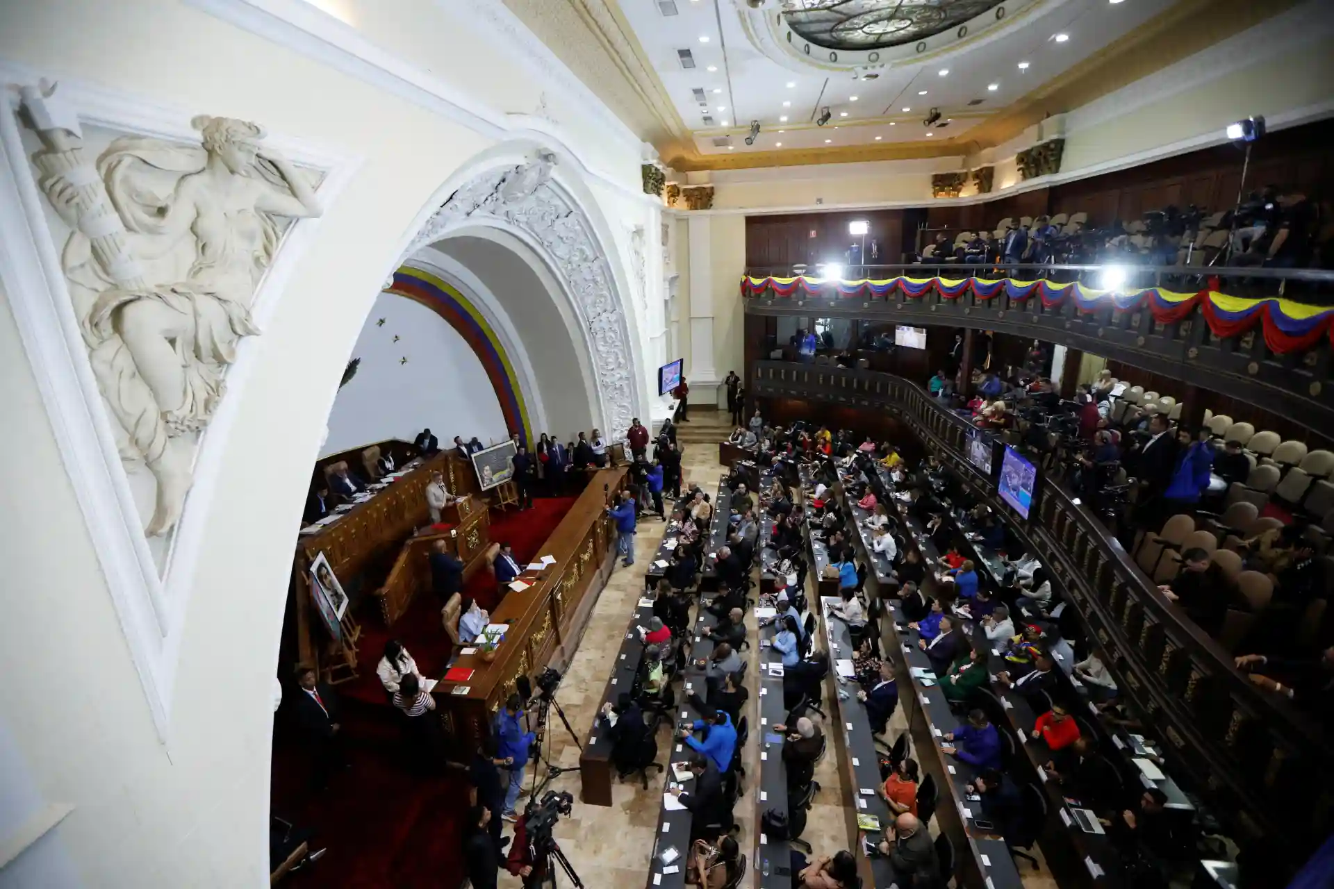 Sessão do Parlamento Nacional na cerimônia oficial, com deputados e autoridades presentes no plenário, decorado com bandeiras e detalhes arquitetônicos tradicionais.