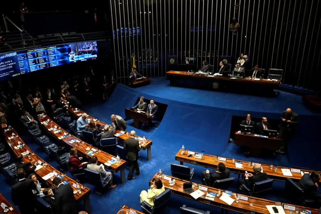 Sessão no plenário do Congresso Nacional do Brasil, com parlamentares e autoridades discutindo projetos de lei, ambiente formal com iluminação adequada e computadores na mesa.