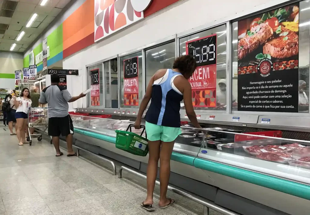 Cliente escolhendo cortes de carne na seção de açougue de supermercado, buscando qualidade e preço justo para fazer uma boa alimentação.