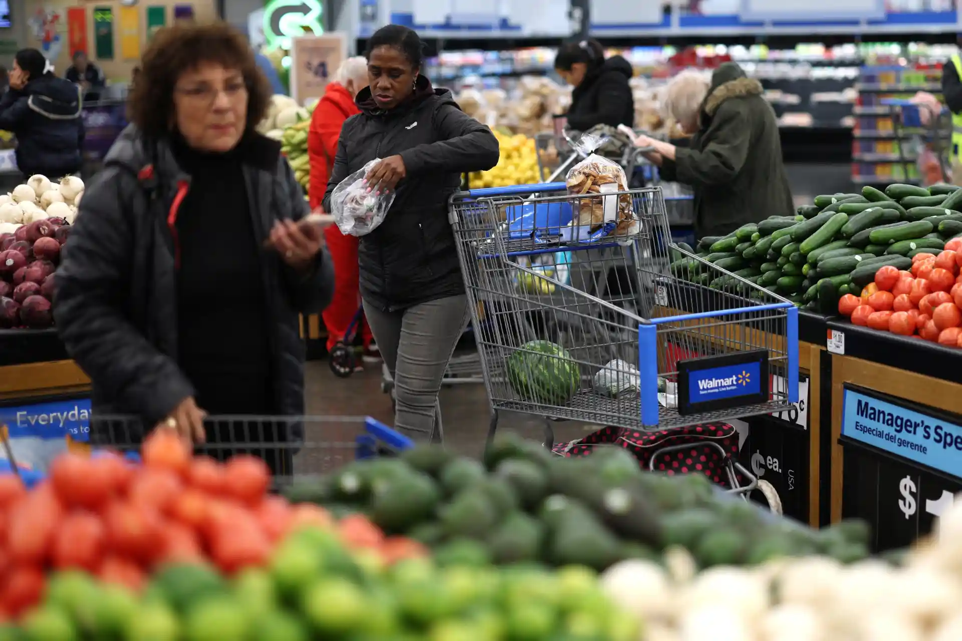Clientes fazendo compras de hortifruti em supermercado Walmart, com destaque para legumes e verduras frescos nas bancadas.